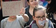 Eine Frau mit zugeklebtem Mund und eine, die en Plakat hochhält, laufen auf einer Demonstration