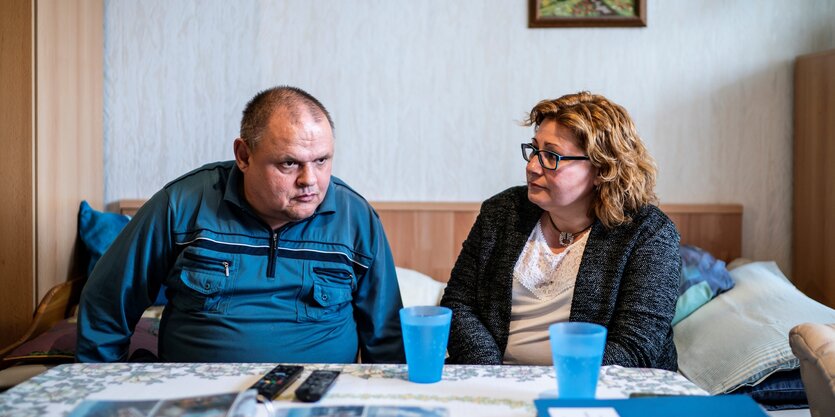 Ein Mann und eine Frau sitzen nachdenklich an einem Tisch in einer aufgeräumten Wohnung