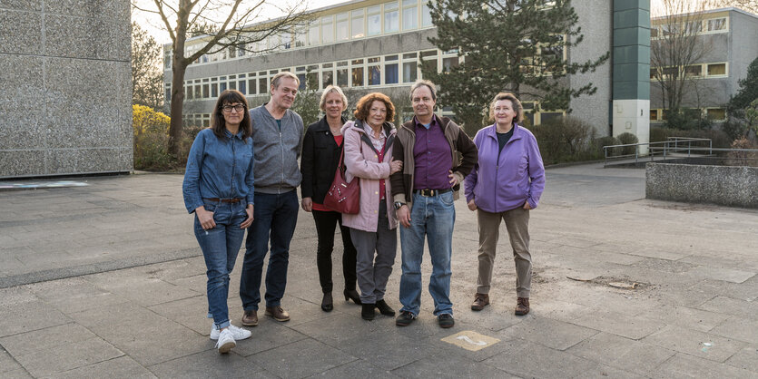 Sechs Menschen stehen vor grauen Schul-Gebäuden.