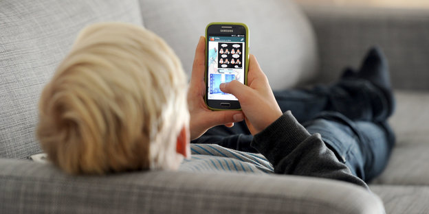 Ein Jugendlicher liegt auf einem Sofa und schaut auf sein Smartphone in seiner Hand