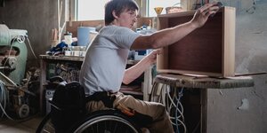 Ein junger Mann im Rollstuhl in einer Tischlerei bei der Arbeit