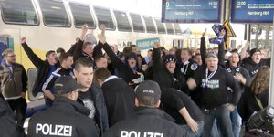 Eine Gruppe männlicher Fußballfans steht brüllend Polizisten gegenüber am Bahnhof