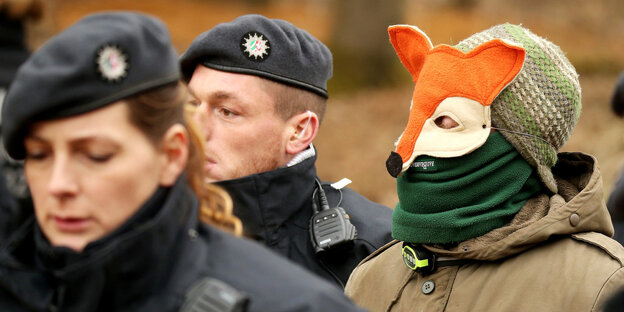 Eine Person mit Fuchsmaske zwischen Polizisten