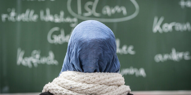 Eine Schülerin mit Kopftuch sitzt im Unterricht vor einer Tafel
