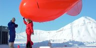 Eine Forscherin und ein Forscher in Schneeanzügen starten einen Wetterballon.