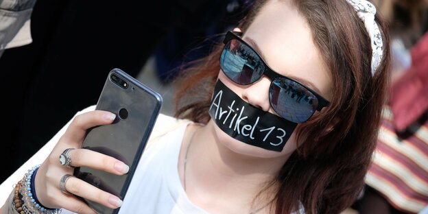 Teilnehmerin einer Demonstration unter dem Motto ·Save the Internet· guckt in ihr Handy