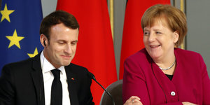 Macron und Merkel sitzen nebeneinander