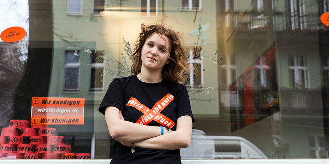 Junge Frau steht vor einem Schaufenster. Auf ihrem T-Shirt steht "unfuck the world"