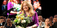 Zuzana Caputova steht lächelnd auf einer Bühne, in den Händen ein Blumenstrauß.