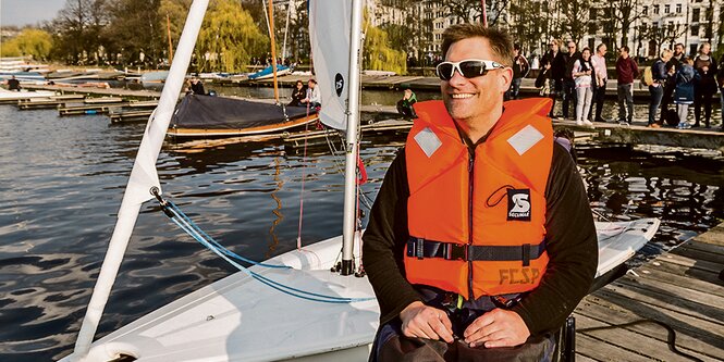 Taufpate Dirk Thalheim sitzt vor dem inklusiven Segelboot des FC St. Pauli.