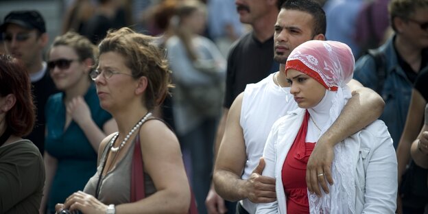 Zuschauer unter freiem Himmel: darunter eine ältere weiße Dame in kurzem Tshirt und ein jüngeres Pärchen, sie mit Kopftuch