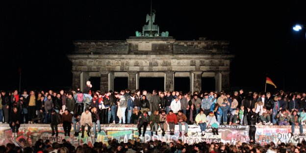 Jubelnde Menschen auf der Berliner Mauer am Brandenburger Tor.