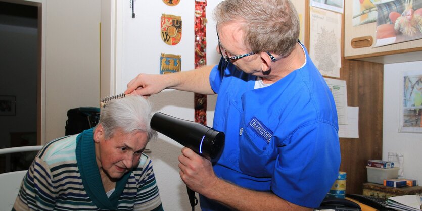 Altenpfleger föhnt alter Dame die Haare