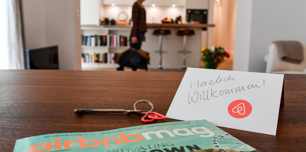 Ein Schlüssel mit einem Airbnb-Anhäger, ein Airbnbmag-Magazin und eine Herzlich-Willkommen-Karte liegen in der Wohnung eines Airbnb-Gastgebers