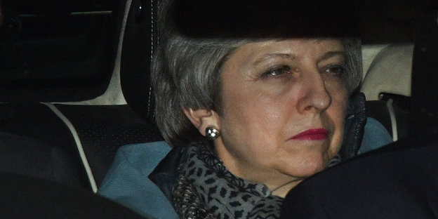 Eine Frau sitzt in einem Auto. Sie guckt ernst. Es ist Theresa May