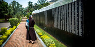 Ein Moench spaziert entlang der Wand des Genozid-Memorials in Ruanda