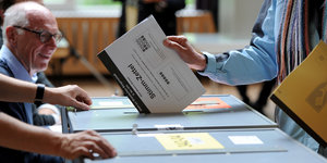 Eine Person steckt einen Wahlzettel in eine Wahlbox.