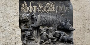 Eine steinerne Plastik zeigt einen Rabbiner, der unter ein Schwein schaut, Menschen saugen an den Zitzen des Schweins