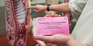 Vor einer Schweinehälfte zeigt ein Schlachter ein Schild mit der Aufschrift "vorläufig sichergestellt"