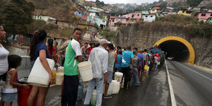 Menschen stehen mit leeren Kanistern in einer langen Schlange vor einer Wasserausgabestelle in Caracas, Venezuela
