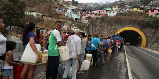 Menschen stehen mit leeren Kanistern in einer langen Schlange vor einer Wasserausgabestelle in Caracas, Venezuela