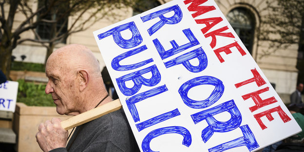Mann mit Schild, darauf steht in rot und blau: "Make the Report public"