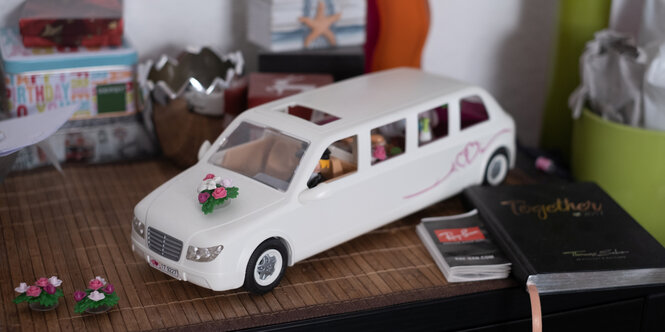 Ein weißes Spielzeugauto, auf dessen Motorhaube ein Blumenbouquet, wie bei einer Hochzeit befestigt ist