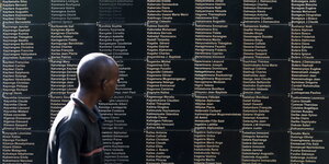Ein Mann steht vor dem Mahnmal, das an den Völkermord erinnert, darauf sind etliche Namen aufgelistet.