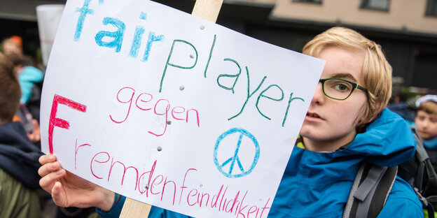 Ein Schüler hält bei einer Demonstration ein Schild mit der Aufschrift "fairplayer gegen Fremdenfeindlichkeit" hoch.