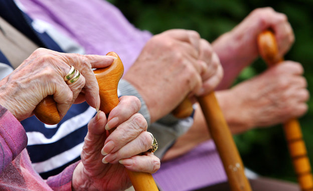 Senioren sitzen auf einer Parkbank und halten ihre Gehstöcke