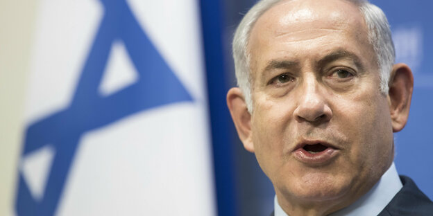 Benjamin Netanjahu, ein älterer Mann mit grauen Haaren vor einem weiß-blauen Hintergrund