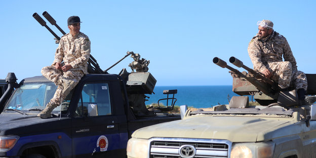 Zwei Männer in Militärkleidung sitzen auf ihren Pick-Ups