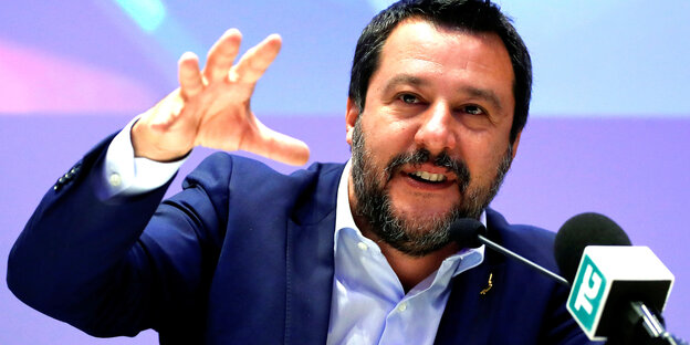 Matteo Salvini - vor ihm befindet sich ein Mikrofon, er greift mit seiner rechten Hand in Richtung Kamera