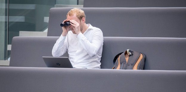 Ein Journalist beobachtet die Sitzung des Bundestages mit dem Fernglas von der Pressetribüne aus.