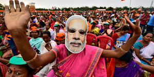 Eine Frau in pinkem Gewand steht in einer Menschenmenge und trägt eine Maske Narendra Modis