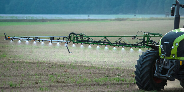 Ein Traktor fährt über ein Feld und spritzt Dünger und Pestizide.