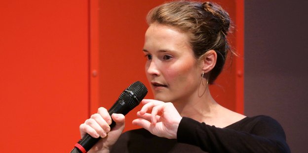 Eine Frau vor rotem Hintergrund spricht in ein Mikrofon
