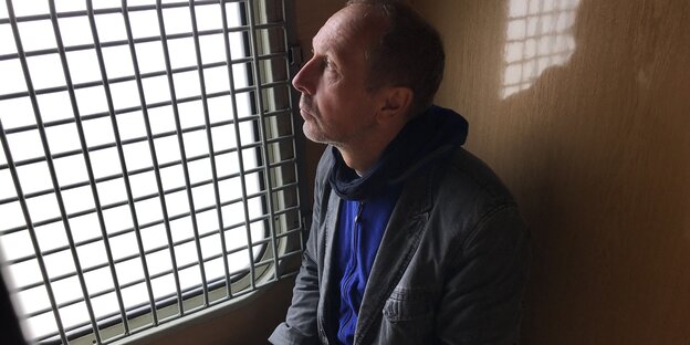 Mittelter Mann schaut auf ein vergittertes Fenster Mittelter Mann schaut auf ein vergittertes Fenster