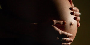 Der Bauch einer schwangeren Frau und ihre darauf liegenden Hände