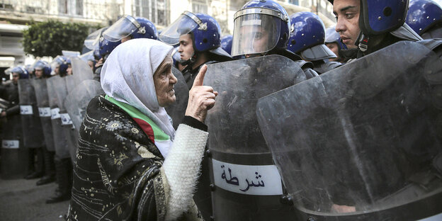 eine alte Dame mit Kopftuch wendet sich an einen Polizisten in einem Spalier von uniformierten Beamten mit Helmen
