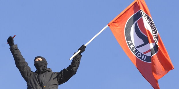 Schwarz gekleideter Antifaschist mit Antifa-Fahne in der Hand