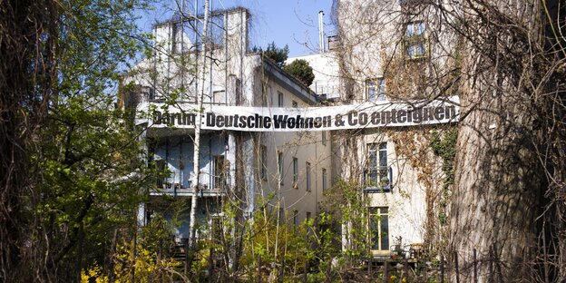Ein Haus hinter Grünpflanzen, darauf ein Banner "Deutsche Wohnen & Co. enteignen"