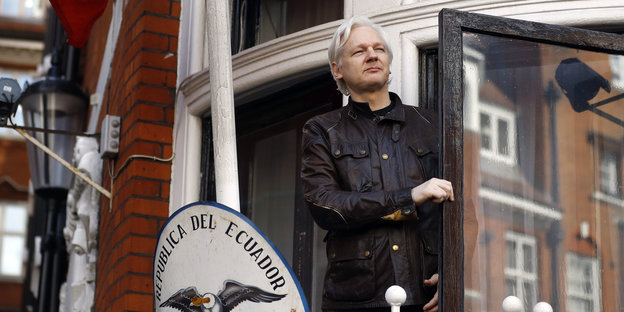 Julian Assange in Lederjacke aus einer Balkontür schauend