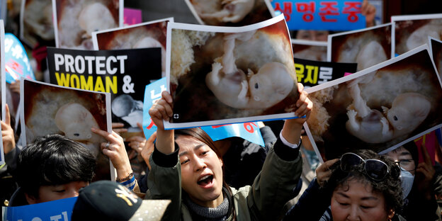 Demonstrant*innen in Seoul halten Schilder und Fotos von Föten hoch