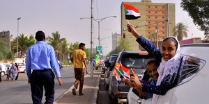 Menschen halten sudanesische Fahnen aus einem Auto