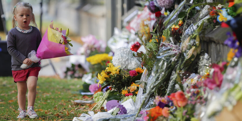 Ein kleines Mädchen trägt Blumen zu einem Gedenkort in Christchurch, Neuseeland