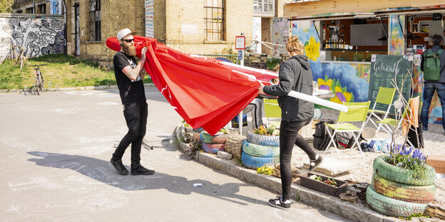 Tobias Burdukats und eine Frau tragen einen roten Sonnenschirm