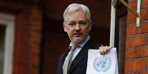 Julian Assange hält eine Papiere mit dem Logo der UN in die Kamera
