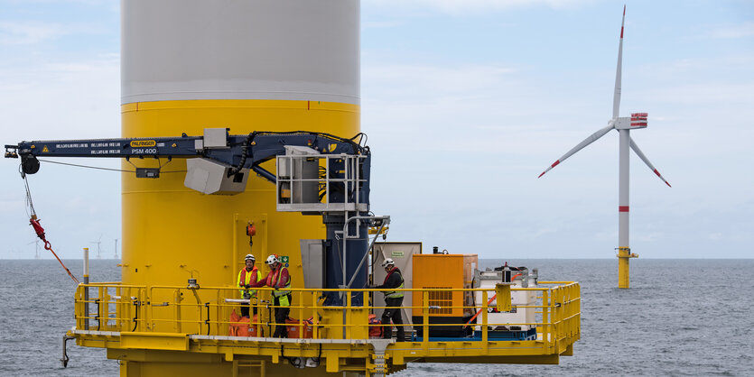 Männer mit Schutzhelmen arbeiten an einer Windkraftanlage auf See