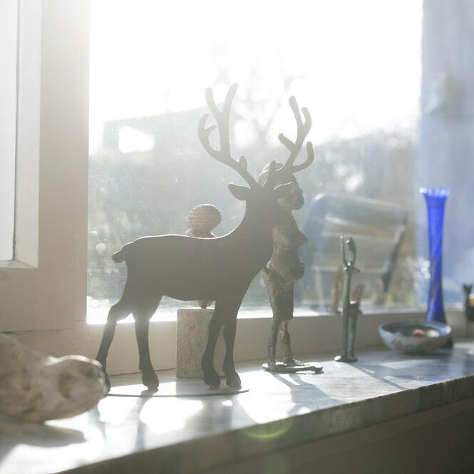 Ein Deko-Hirsch steht auf einer Fensterbank. Die Sonne scheint durchs Fenster.